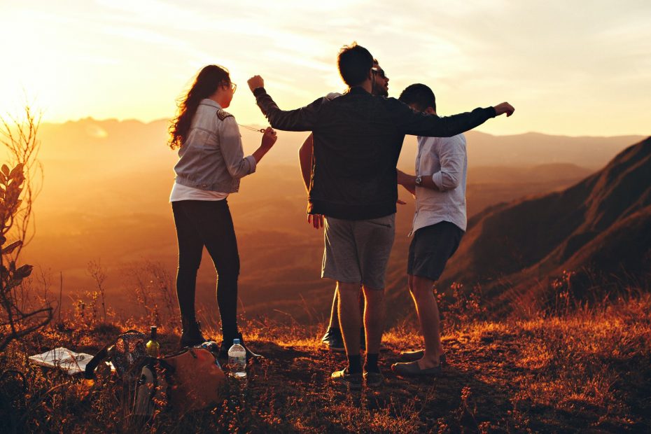 four person standing at top of grassy mountain